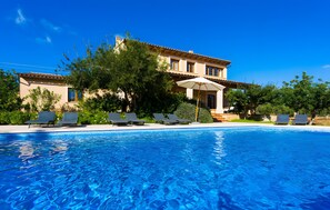 A swimming pool with lounge chairs and an umbrella, surrounded by trees and a building with a tiled roof.