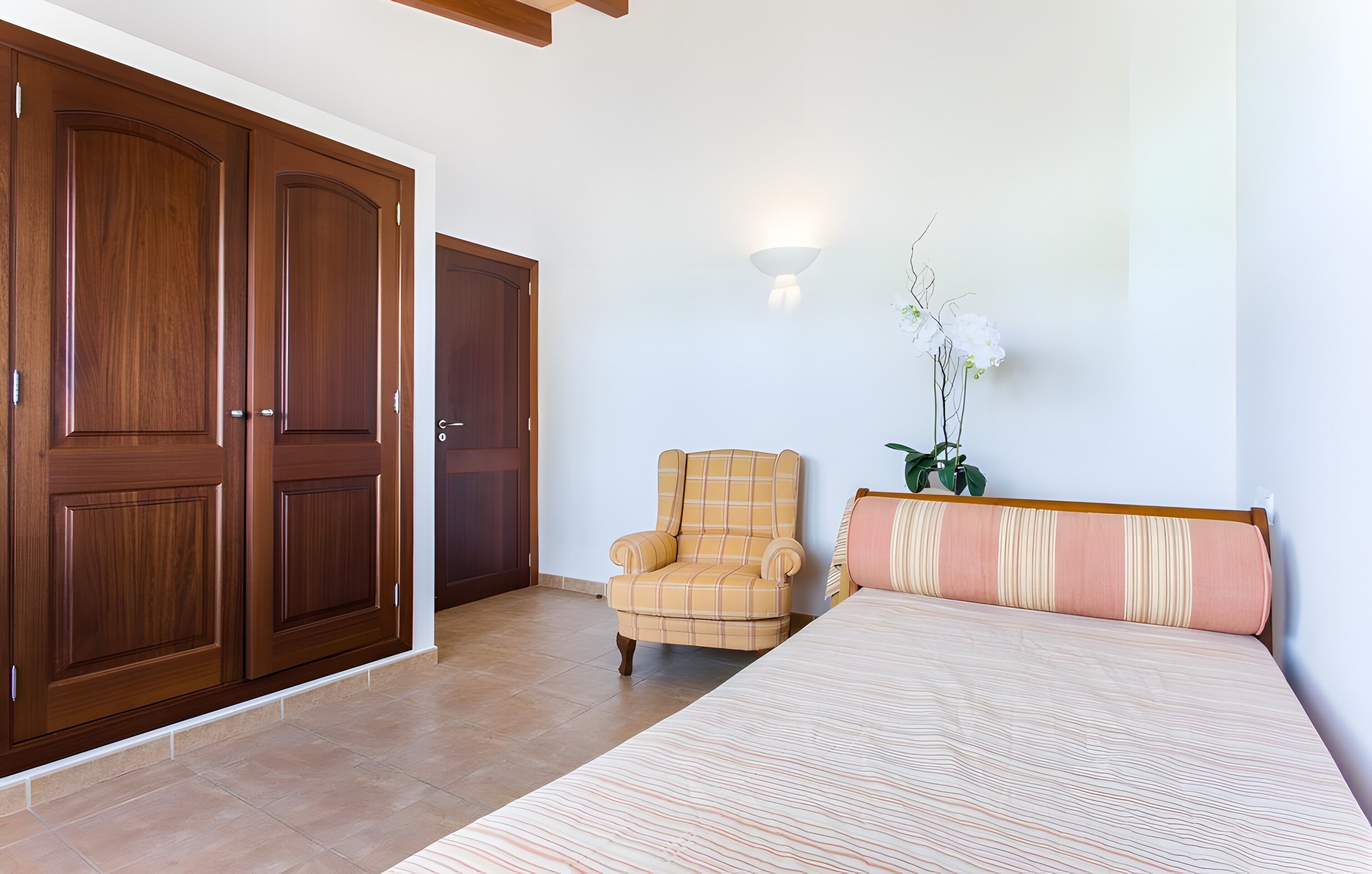 Un dormitorio con cama, una silla, una planta y un armario.