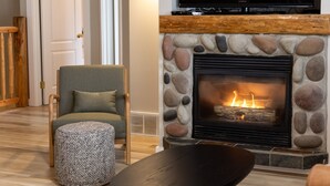 A cozy living room with a stone fireplace, a comfortable armchair, and a round ottoman. - Newly Renovated 3 Bedroom l A/C | Sleeps 8 (Fernie)