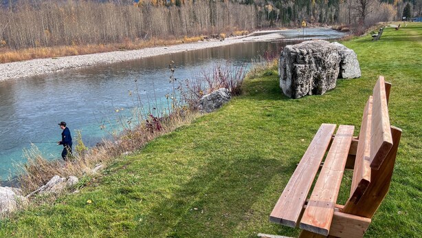 A riverside picnic area with a bench and a person fishing. - Newly Renovated 3 Bedroom l A/C | Sleeps 8 (Fernie)