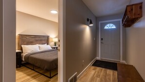 A bedroom with a bed, bedside table, lamp, and a wooden headboard. - Newly Renovated 3 Bedroom l A/C | Sleeps 8 (Fernie)