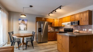 A modern kitchen with wooden cabinets, stainless steel appliances, and a dining area with a round table and chairs. - Newly Renovated 3 Bedroom l A/C | Sleeps 8 (Fernie)