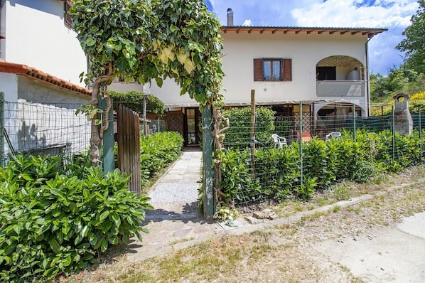 A house with a paved pathway, a wooden fence, and green shrubs.