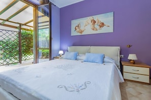 A bedroom with a bed, two bedside tables, a window, and a painting on the wall.