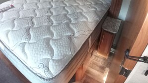 A compact RV bedroom with a bed, wooden headboard, and a small wooden stool. - Luxury 2-bedroom RV in fabulous Woodbury with WiFi, AC (Woodbury)