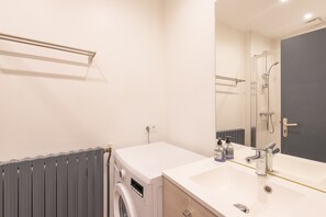 Une salle de bain moderne équipée d’un lave-linge intégré, d’un lavabo avec miroir et d’un espace douche.