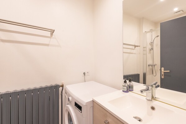 Un baño moderno con lavadora integrada, un lavamanos con espejo y zona de ducha.