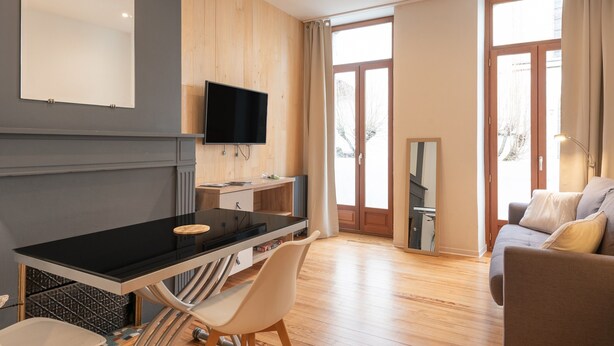 A modern room with a black dining table, white chairs, a TV, and a sofa.