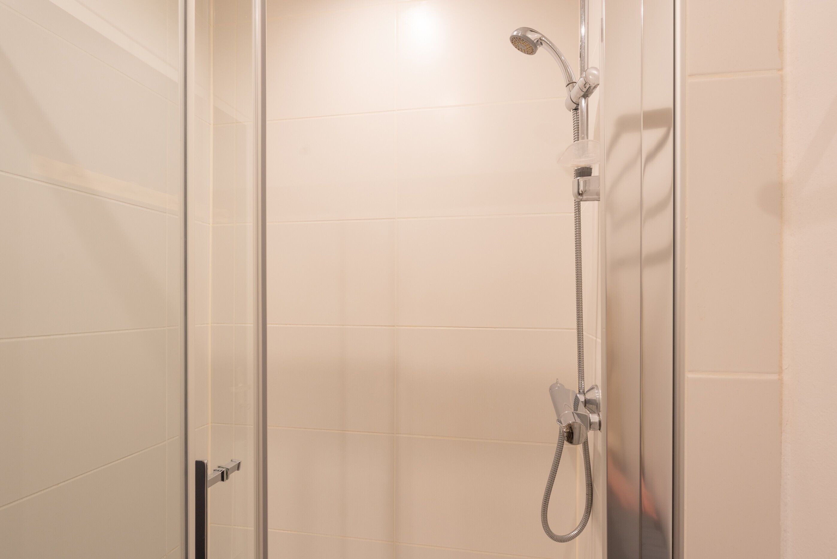 A glass-enclosed shower stall with a handheld showerhead and a wall-mounted faucet.