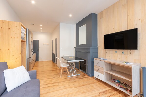 Un salon moderne comprenant un canapé, une table à manger avec des chaises, un téléviseur fixé au mur et une cheminée.