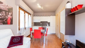 A compact living space with a dining area, kitchen, and a white sofa with a red cushion.