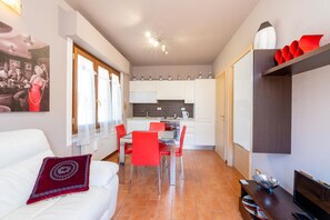 Un espacio habitable compacto con comedor, cocina y un sofá blanco con un cojín rojo.