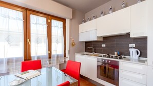 A modern kitchen with white cabinets, a glass dining table, red chairs, and a view through the window.