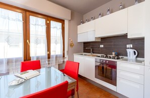 Una cucina moderna con mobili bianchi, un tavolo da pranzo in vetro, sedie rosse e vista dalla finestra.