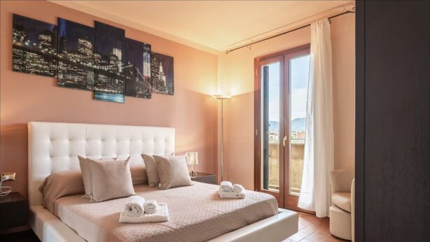 A hotel room with a large bed, a cityscape artwork, a balcony with a view, and a sliding door.