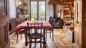 A traditional kitchen with a tiled floor, wooden cabinets, a dining table with chairs, and a bookshelf filled with books. - Charming House with Large Garden – Perfect for Families, Near Pool, Tennis & Nature (La Roche-Chalais)