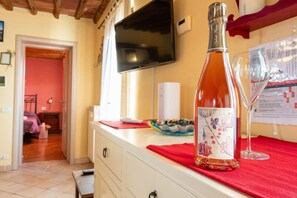 Een kamer met een aan de muur bevestigde televisie, een fles wijn en een glas op een tafel.