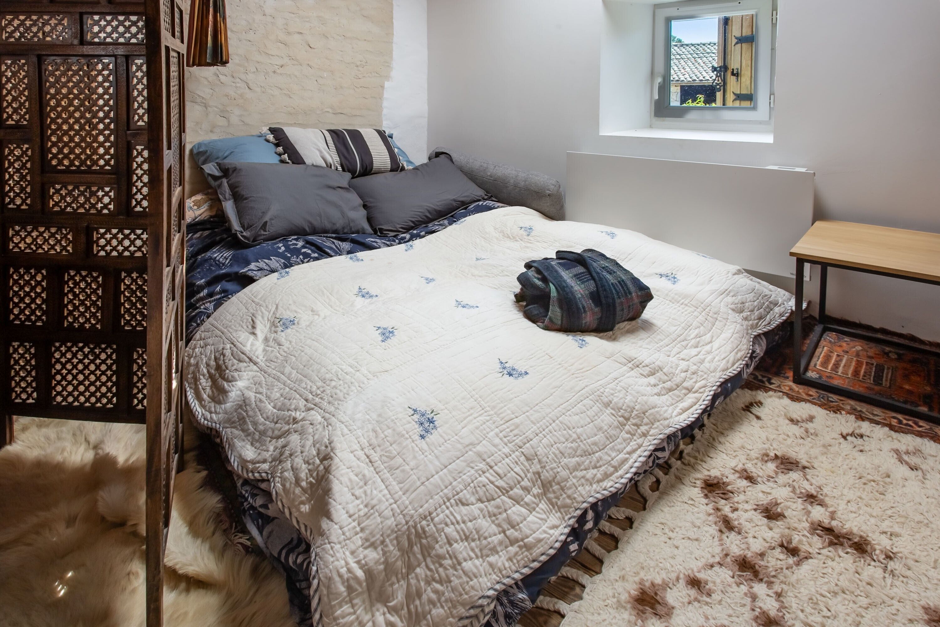 Un dormitorio con cama, ventana, mesa de madera y alfombra de piel.