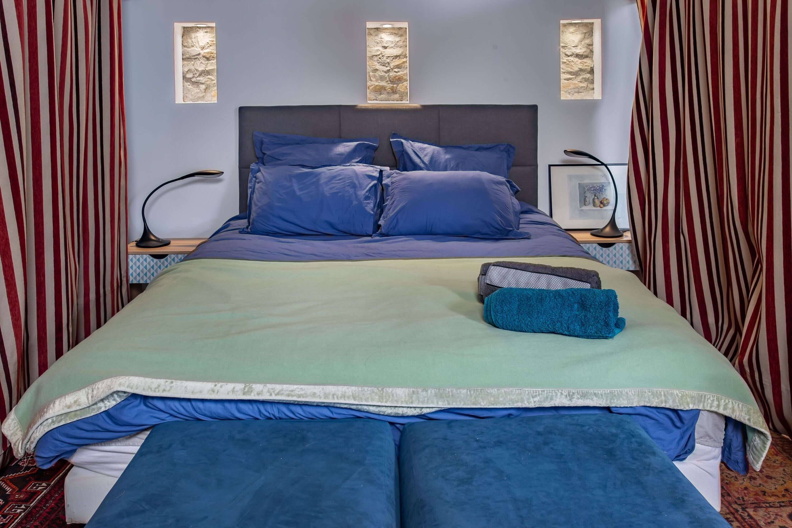 A neatly made bed with blue bedding, a headboard, and two bedside tables with lamps.