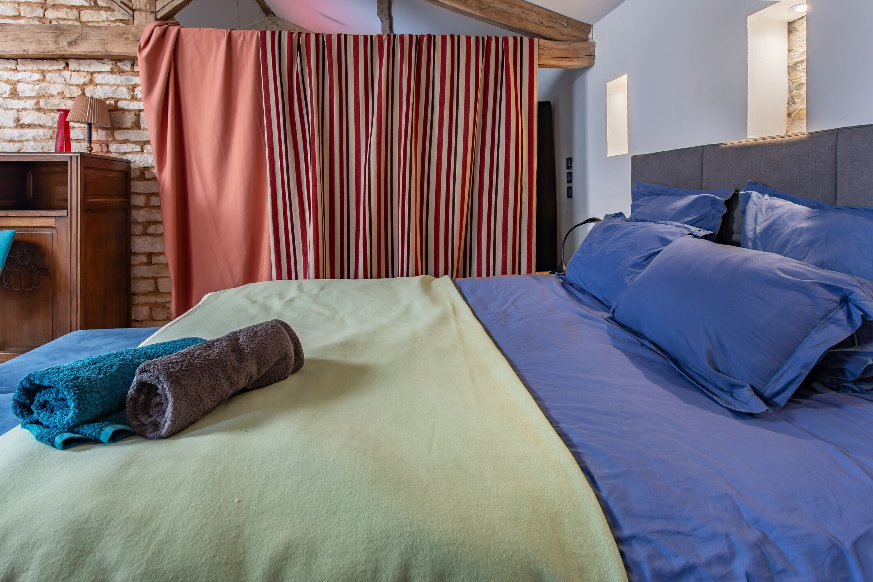 Una cama con ropa de cama azul, una manta verde y una toalla enrollada.