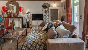 Ein gemütliches Schlafzimmer mit einer geblümten Bettdecke, einem Fernseher, einem beleuchteten Spiegel und einer Tür mit dekorativem Bogen.