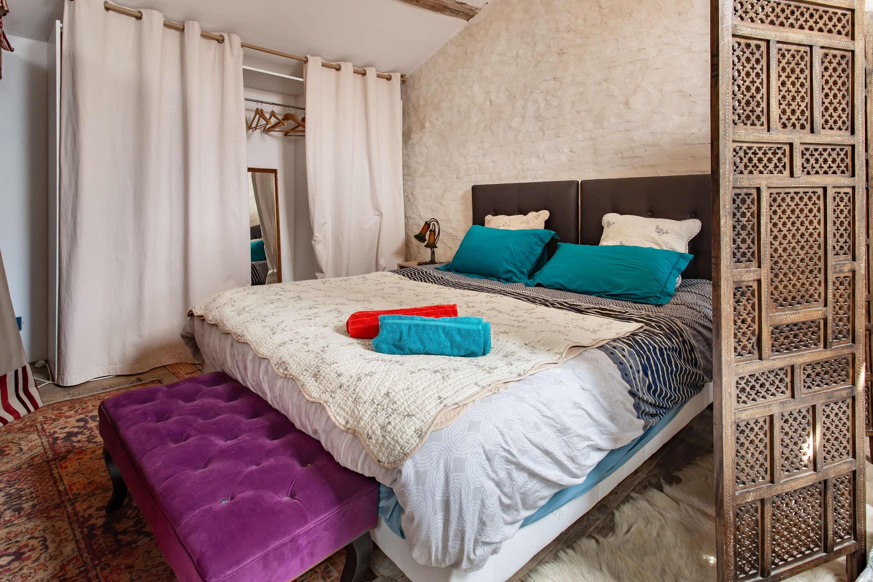 A bedroom with a bed, a purple bench, a wooden partition, and a patterned rug.