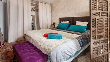 A bedroom with a bed, a purple bench, a wooden partition, and a patterned rug.