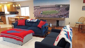 A living room with a large flat-screen TV displaying a football stadium, a sectional sofa, and a coffee table.