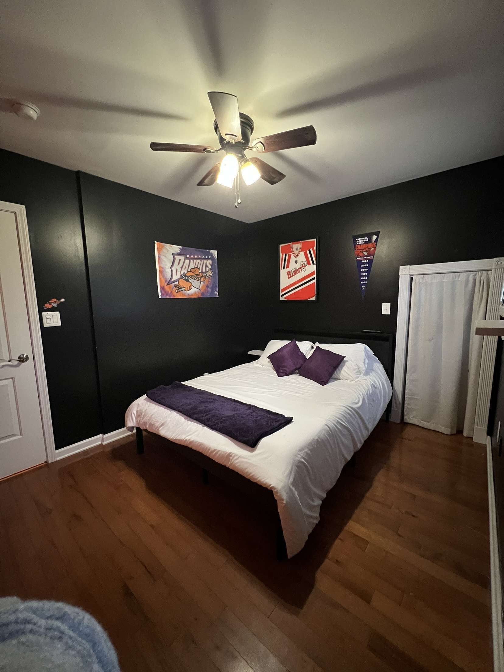 Un dormitorio con una cama, un ventilador de techo y dos carteles en la pared.