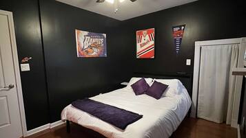 Un dormitorio con una cama, un ventilador de techo y dos carteles en la pared.