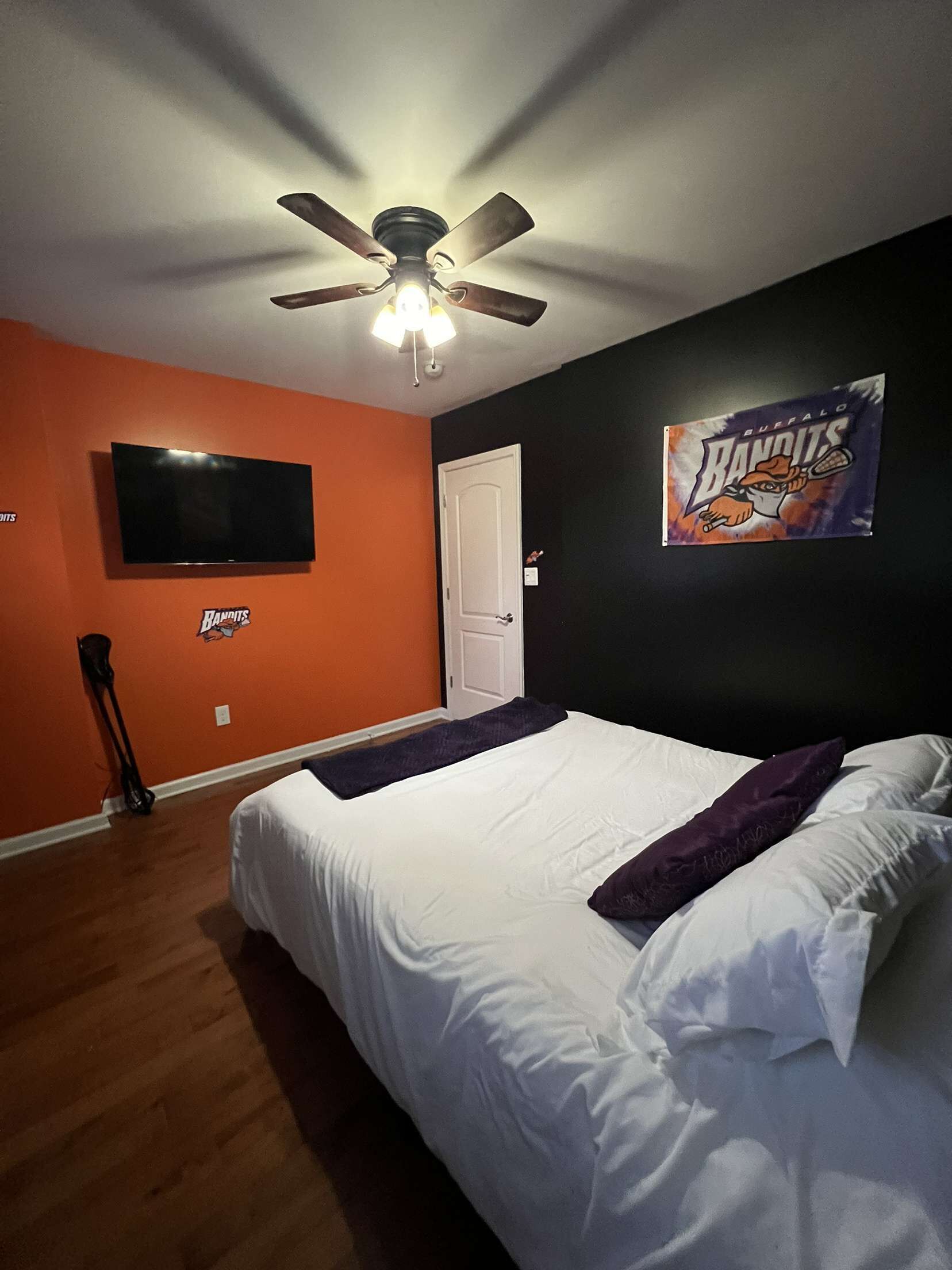 Un dormitorio con cama, ventilador de techo, televisión y una puerta.