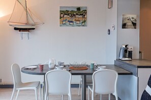 Un coin repas avec une table ronde, des chaises blanches, un luminaire suspendu et des œuvres d’art accrochées aux murs.