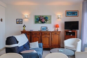 Un salon avec un canapé, un fauteuil, une télévision et des œuvres d’art accrochées au mur.