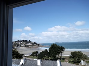 Une vue sur la côte, depuis une fenêtre donnant sur une plage, des maisons et des arbres.