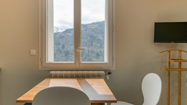A room with a window, a table, a chair, and a television. - Apartment 'Pmr' - Logis les forges (Arvillard)