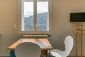 A room with a window, a table, a chair, and a television.