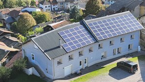 A building with multiple solar panels on the roof, a parking area, and a surrounding residential neighborhood. - Apartment 'Pmr' - Logis les forges (Arvillard)