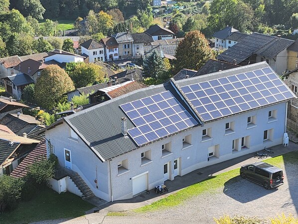 A building with multiple solar panels on the roof, a parking area, and a surrounding residential neighborhood.