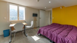 A bedroom with a bed, a desk, a chair, a TV, and a window with a view of trees. - Apartment 'Pmr' - Logis les forges (Arvillard)