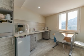 A compact kitchen with a microwave, refrigerator, and sink. There is a window with a view of a forested area.