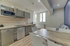 Eine moderne Küche mit integrierten Geräten, ein Essbereich mit einem Holztisch und weißen Stühlen sowie ein Fenster, das für natürliches Licht sorgt.