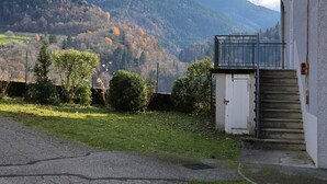 Un edificio con una scala che conduce a una porta, un'area recintata con alberi e una montagna sullo sfondo.