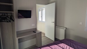 Quarto com cama, televisão na parede, guarda-roupa, secretária e radiador.