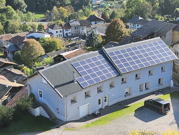 A building with multiple solar panels on the roof, a parking area, and a surrounding residential neighborhood.
