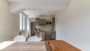 Een moderne keuken met inbouwapparatuur, een eethoek met een houten tafel en stoelen, en een zichtbaar raam.