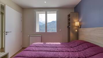 A bedroom with a bed, a window with a mountain view, a radiator, and a wall-mounted shelf.