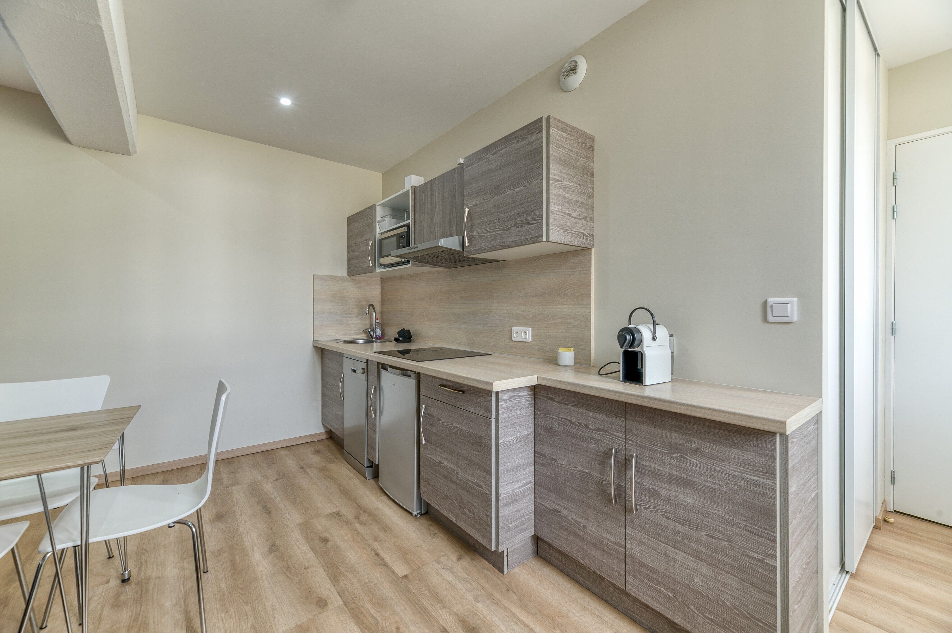 A compact kitchen with built-in appliances, a dining area with a table and chairs, and a light-colored floor.