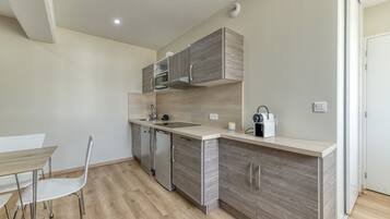 A compact kitchen with built-in appliances, a dining area with a table and chairs, and a light-colored floor.