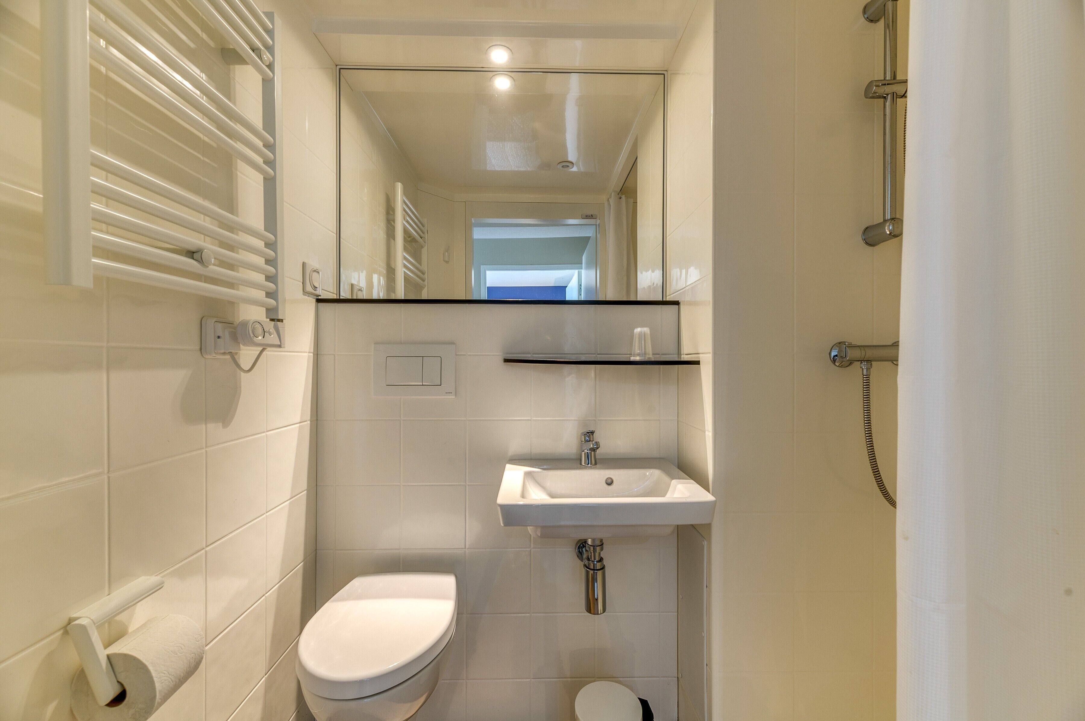 A bathroom with a toilet, sink, mirror, and towel rack.