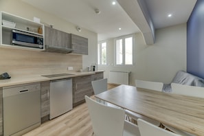 A modern kitchen with built-in appliances, a dining area with a wooden table and white chairs, and a window providing natural light.
